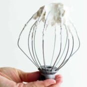 Someone holding a stand mixer whisk attachment with homemade whipped cream on the end.