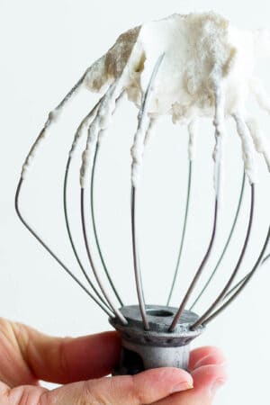 Someone holding a stand mixer whisk attachment with homemade whipped cream on the end.