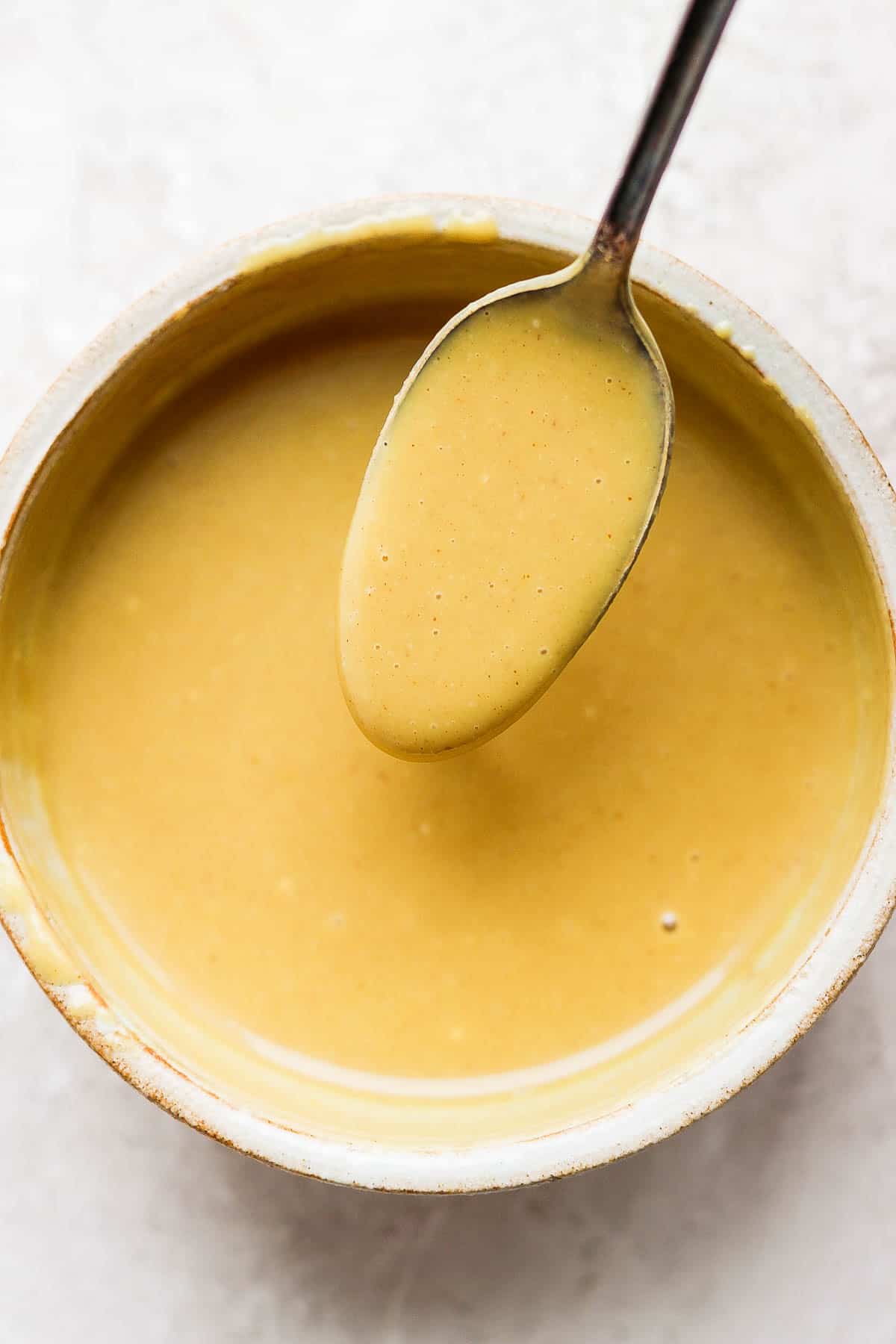 A small bowl of honey mustard with a spoon.