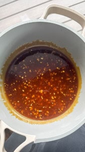 Someone holding a medium sauce pan next to a window filled with thick, homemade teriyaki sauce inside. 