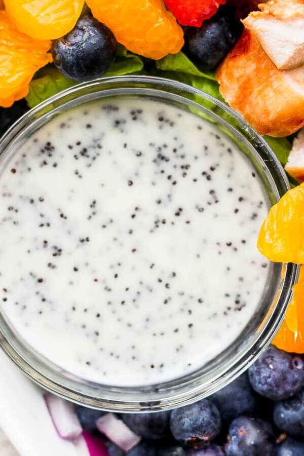Little bowl of poppyseed dressing sitting inside a salad bowl with ingredients around it.