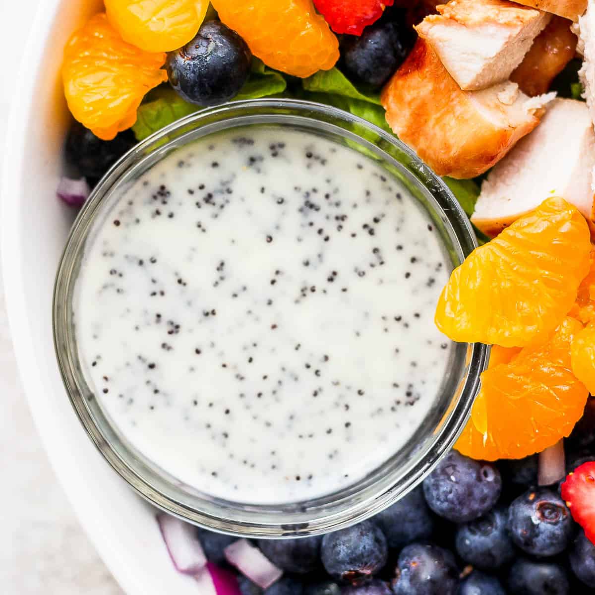 Little bowl of poppyseed dressing sitting inside a salad bowl with ingredients around it.