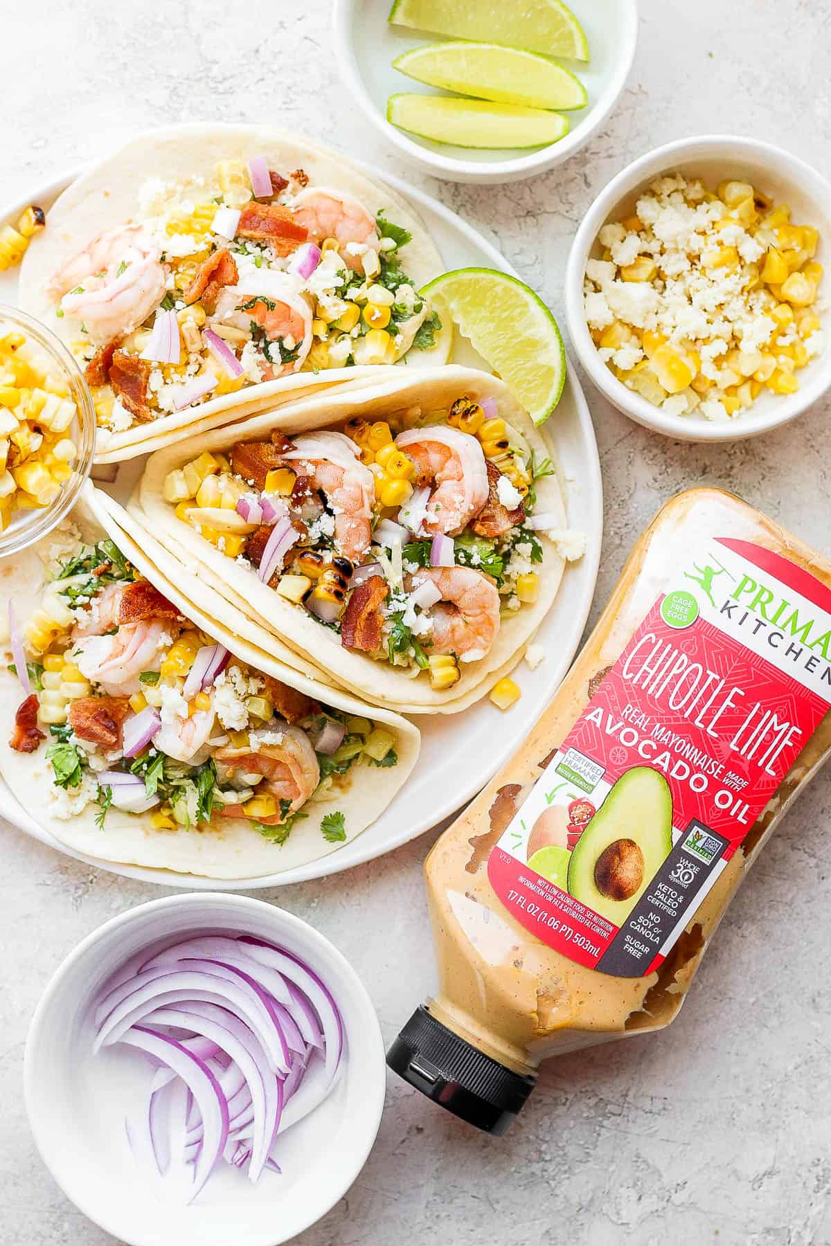 Three shrimp tacos on a plate next to a bottle of Primal Kitchen's chipotle lime mayo. 