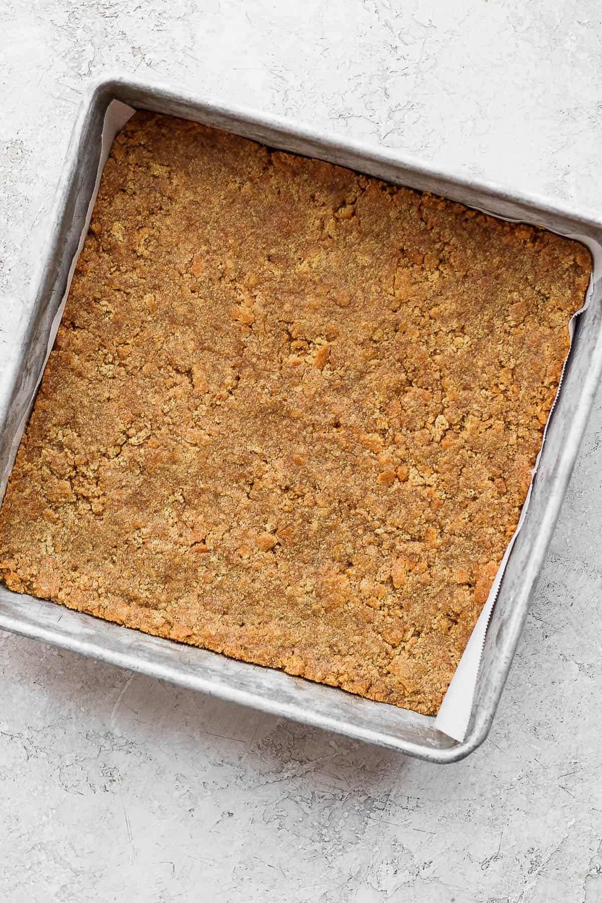 Graham cracker crust pushed into a parchment-lined baking pan.