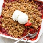 Top view of a pan of strawberry crisp with two spoons sticking out and a scoop of ice cream on top.