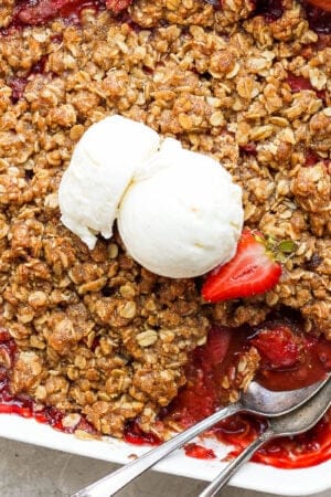 Top view of a pan of strawberry crisp with two spoons sticking out and a scoop of ice cream on top.