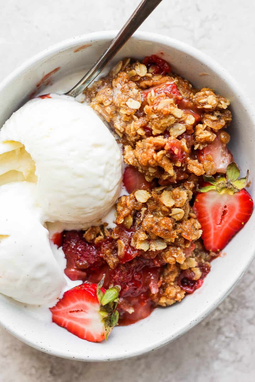 Strawberry crisp in a bowl with ice cream.