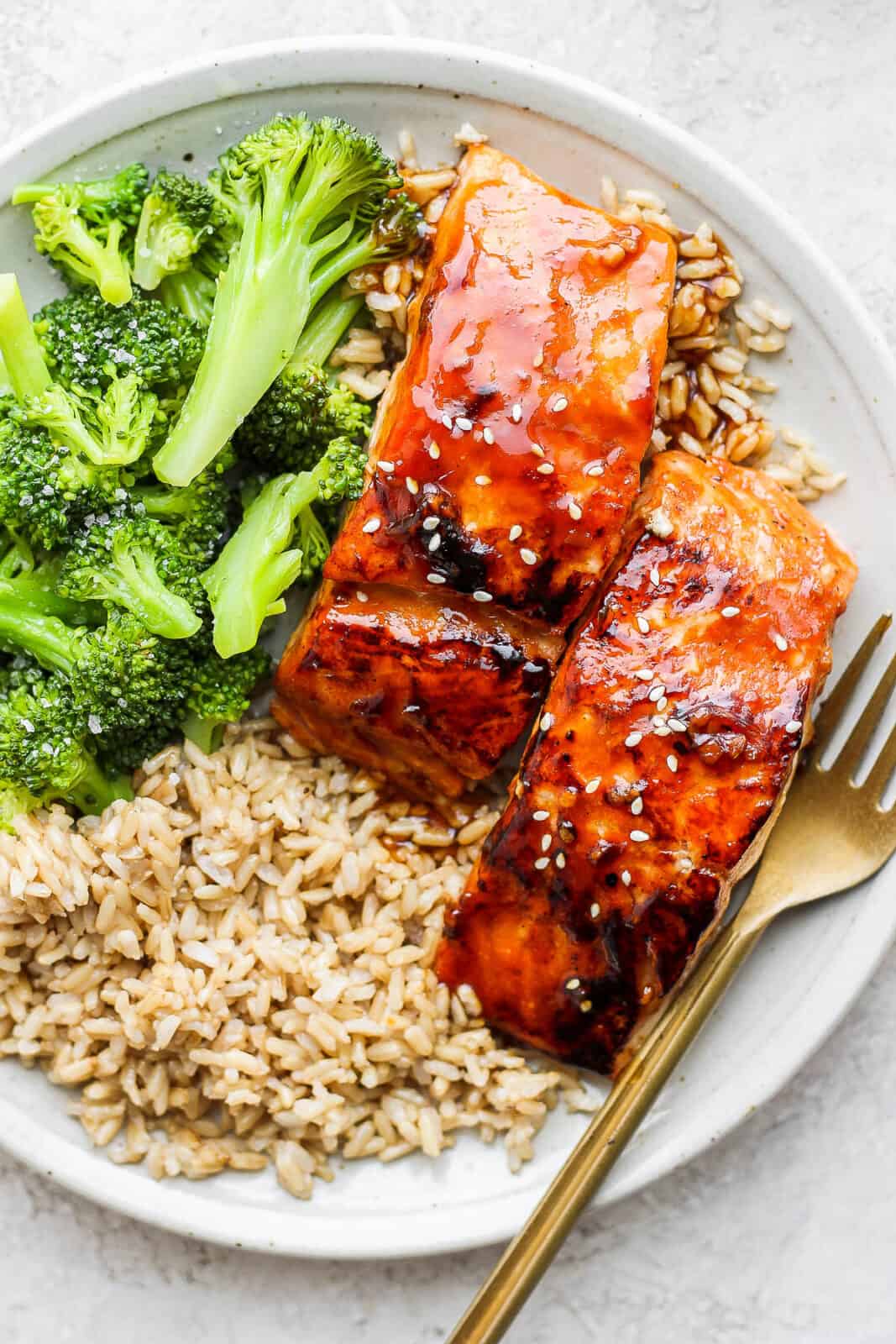 A plate of teriyaki salmon with rice, broccoli, and a fork.