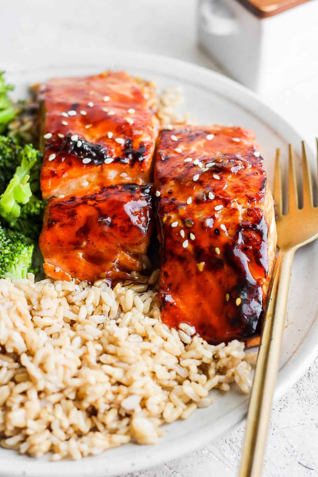 Teriyaki salmon fillets on a plate with rice, broccoli, and a fork.