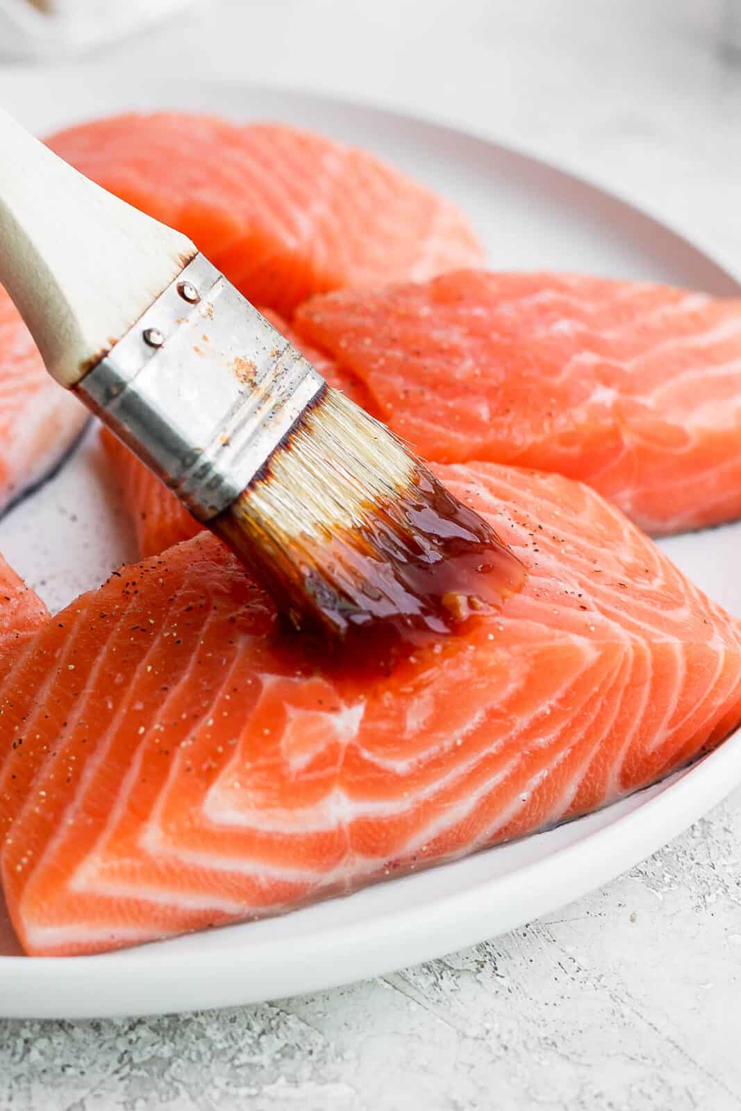 Salmon fillets being brushed with teriyaki sauce.