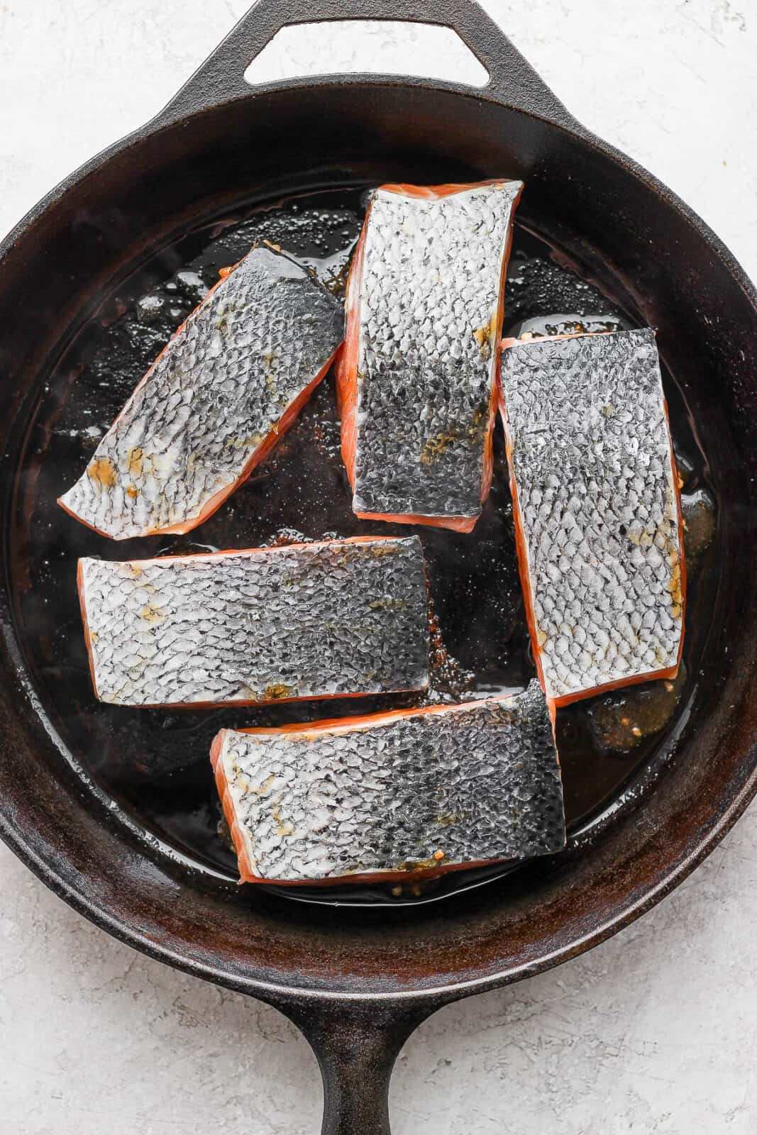 Salmon fillets being seared in a cast iron skillet.