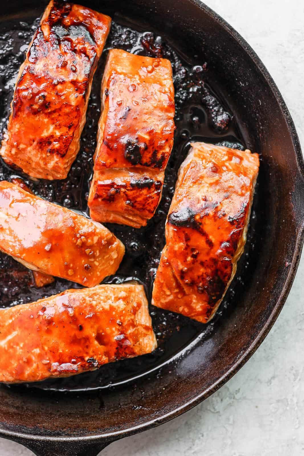 Salmon fillets in a cast iron skillet with more teriyaki sauce on top.