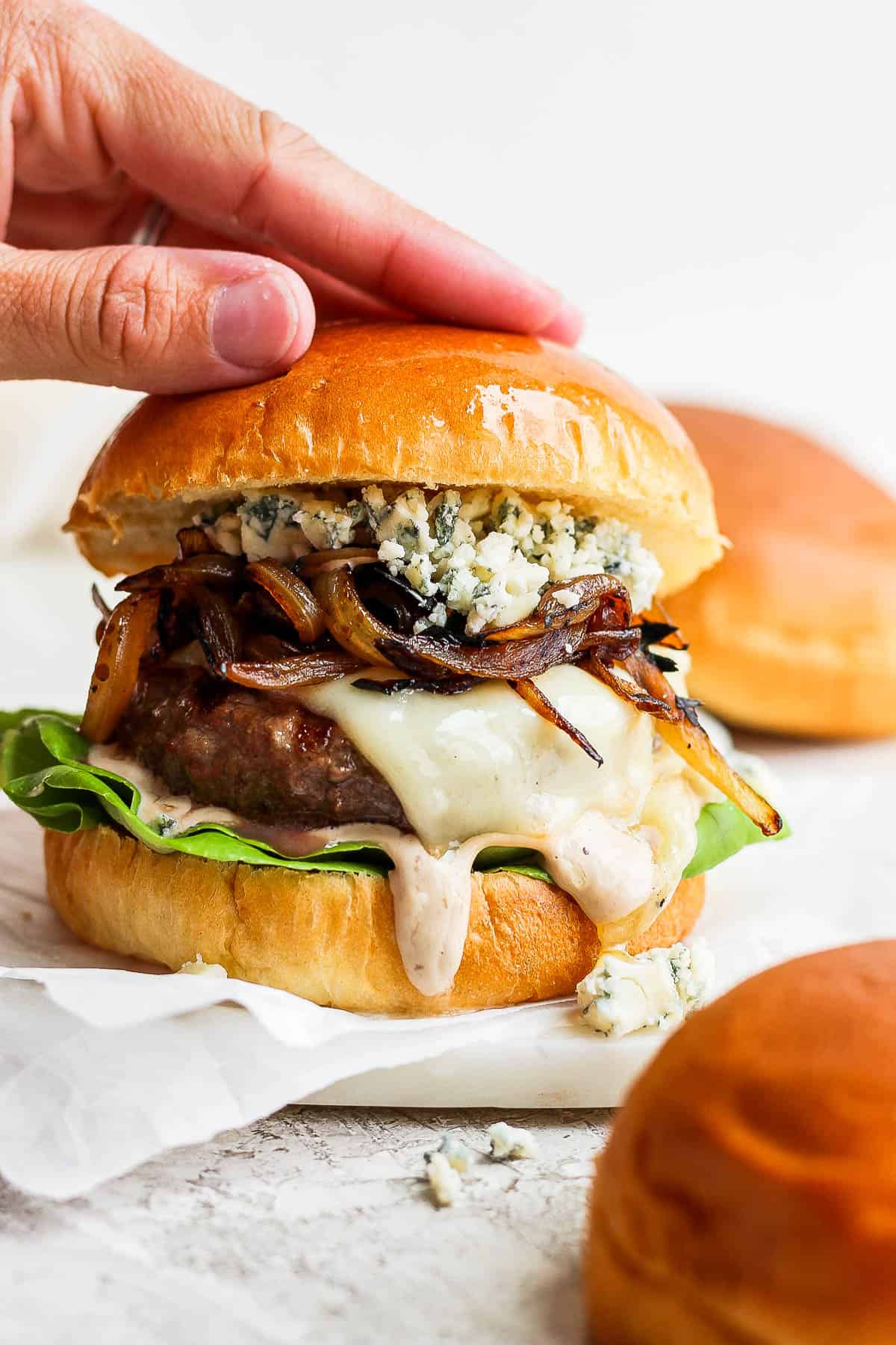 A hand placing the top bun on a bison burger.