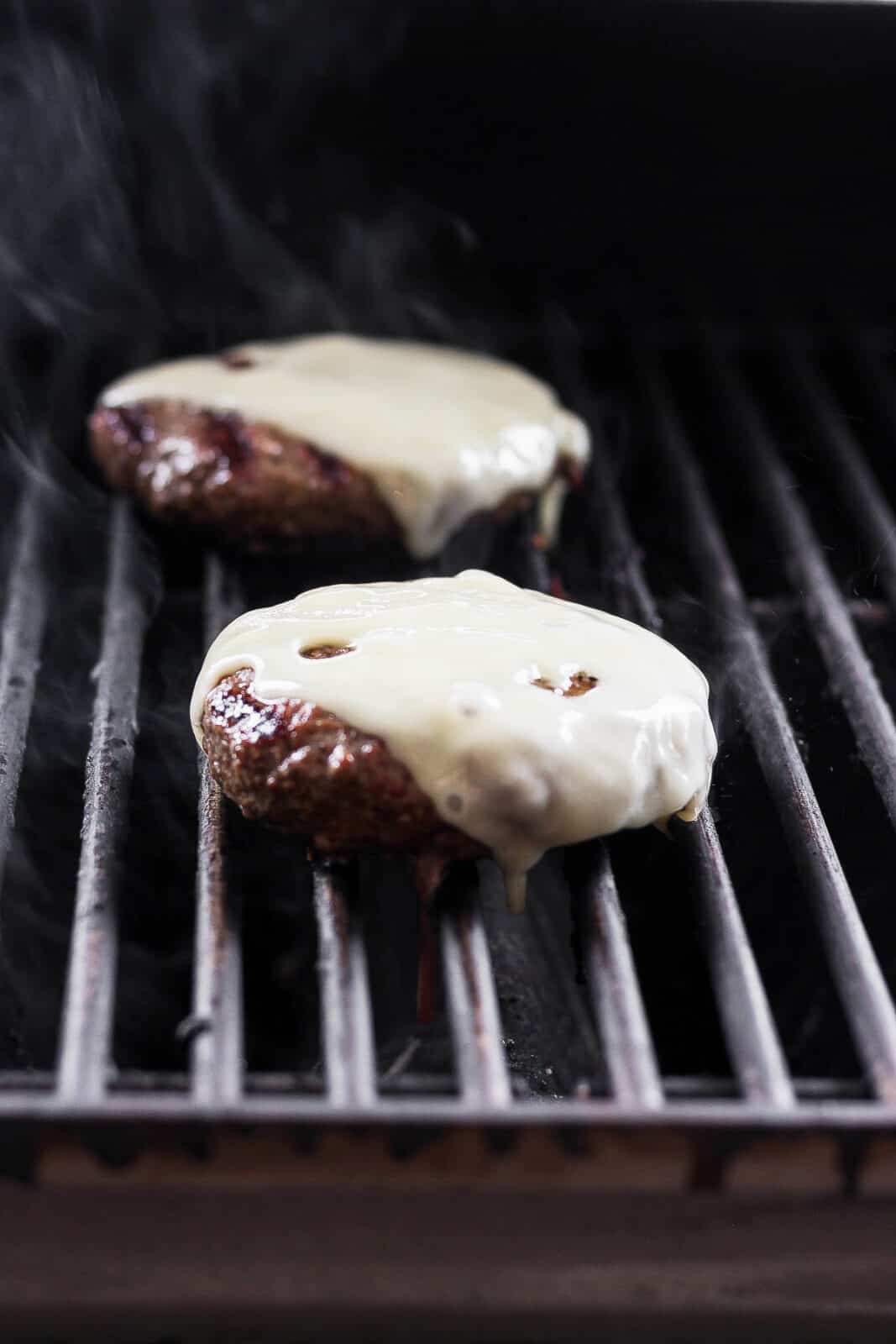 Bison burgers with melted cheese on the grill.