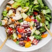 A chopped Greek Chicken Salad in a bowl with two spoon sticking out.