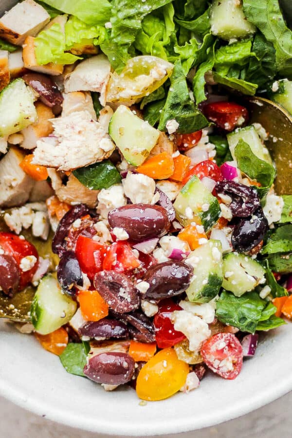A chopped Greek Chicken Salad in a bowl with two spoon sticking out.