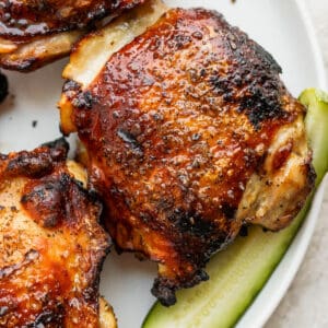 A pickle brined chicken thigh on a plate next to a pickle.