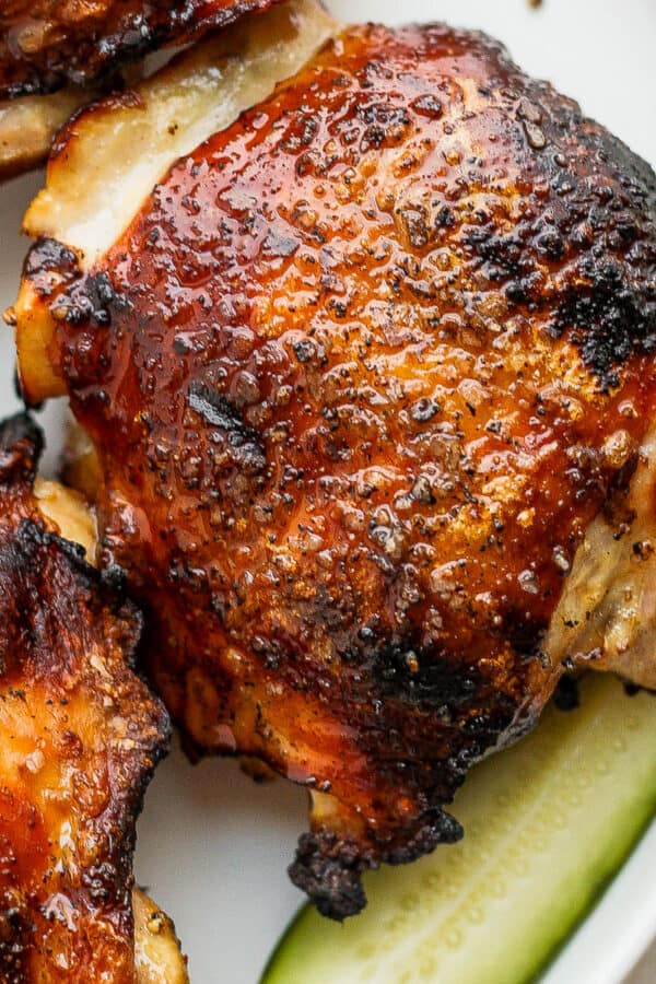A pickle brined chicken thigh on a plate next to a pickle.