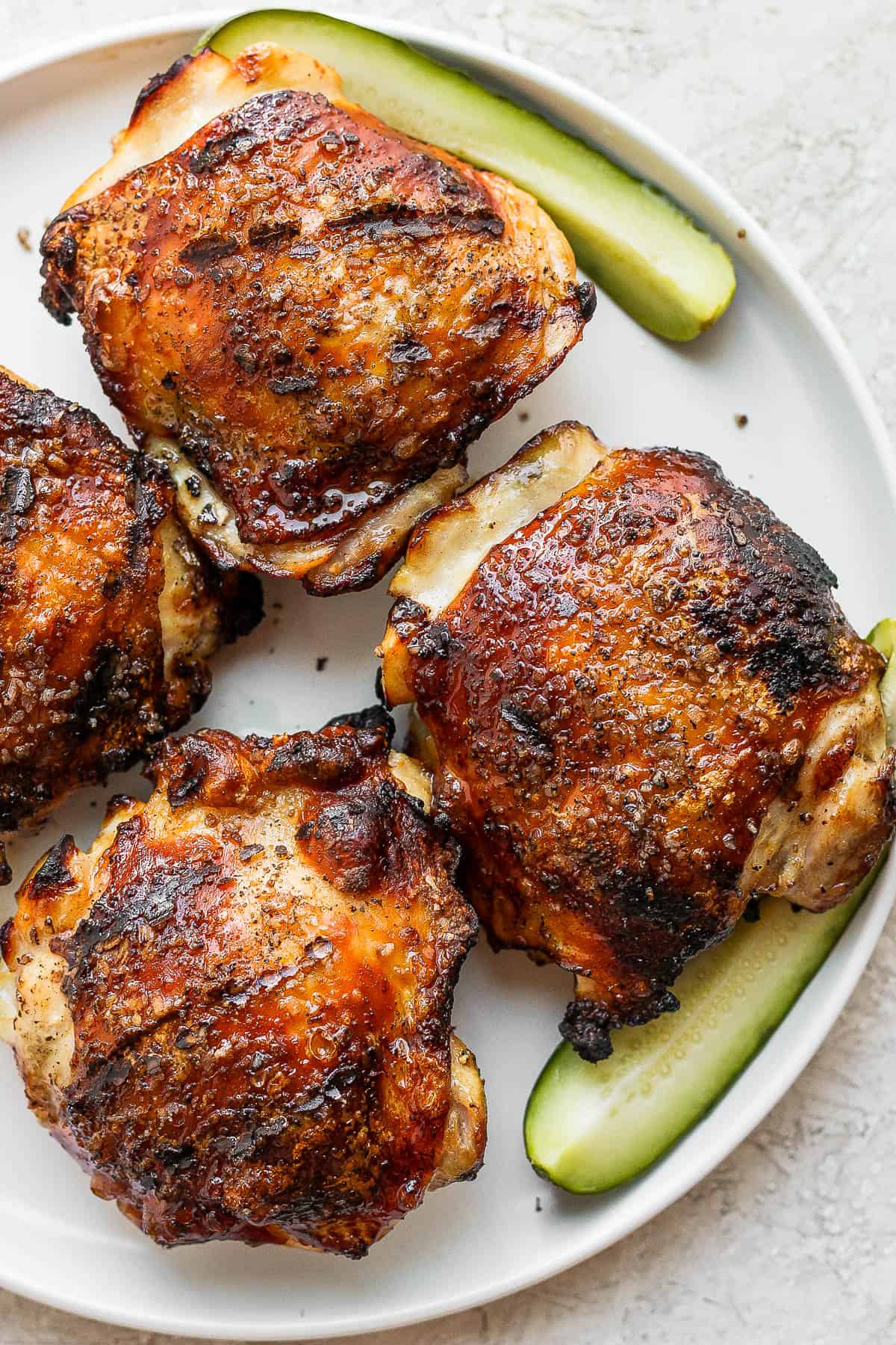 Four chicken thighs on a plate with a pickle spear as a garnish.