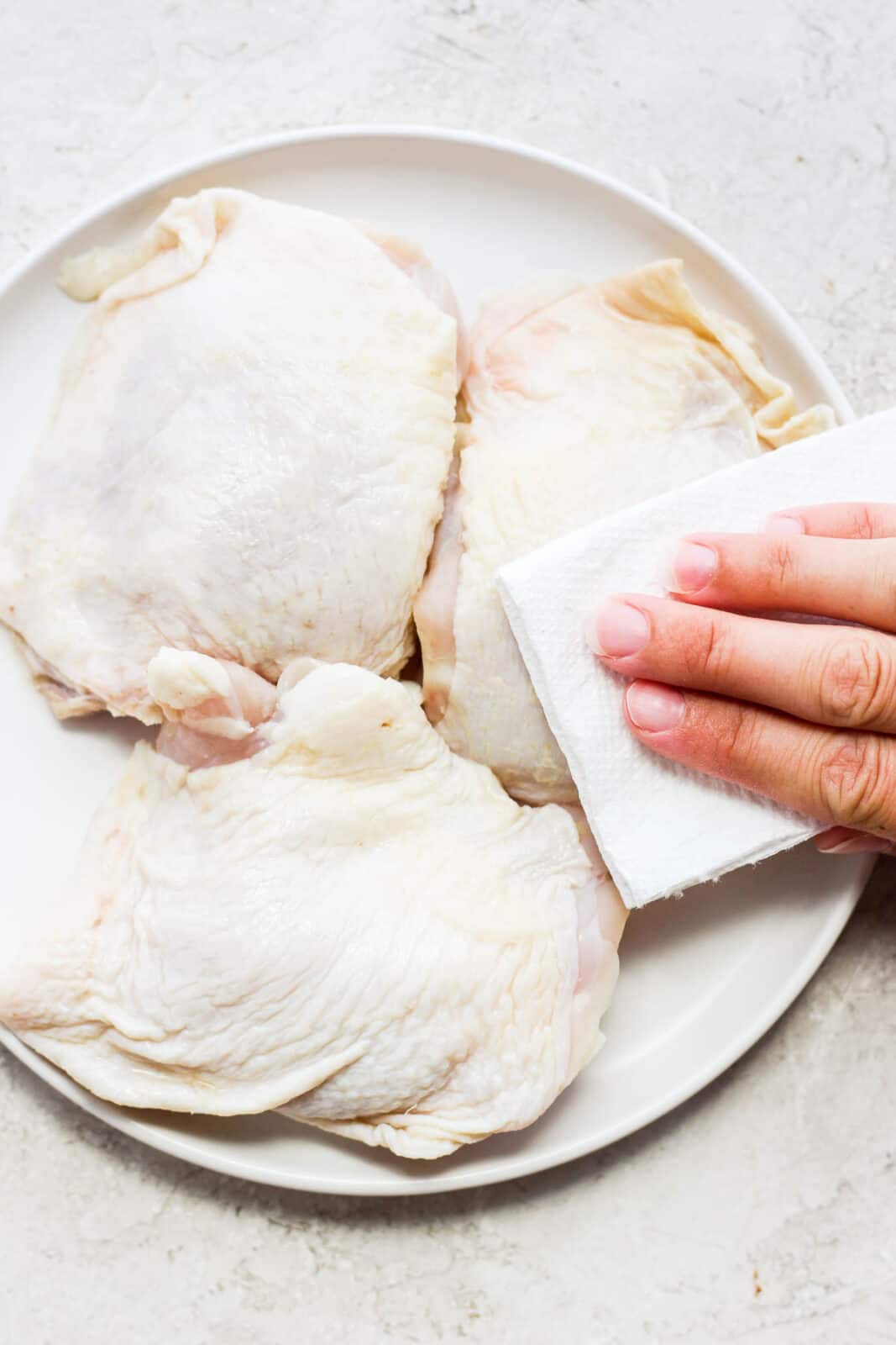 A hand patting dry a chicken thigh with a paper towel.