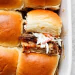 A pan of pulled pork sliders with one flipped on its side so you can see the pork and coleslaw.