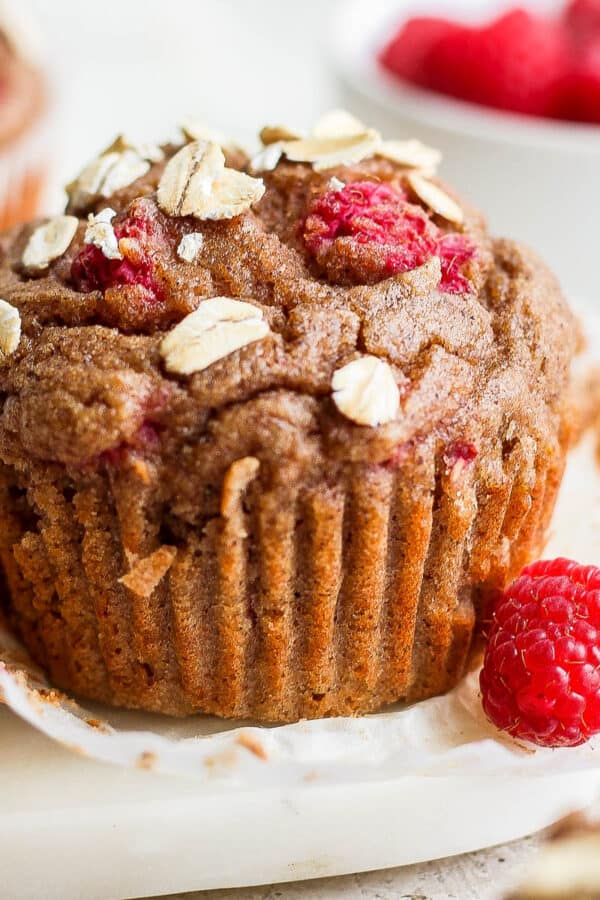 A raspberry muffin with a fresh raspberry next to it.