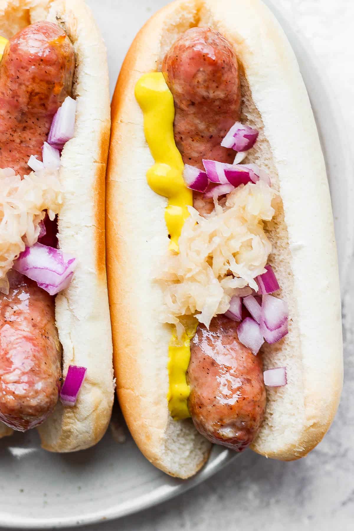 Close up of a juicy smoked brat in a bun and topped with sauerkraut, red onion and mustard.
