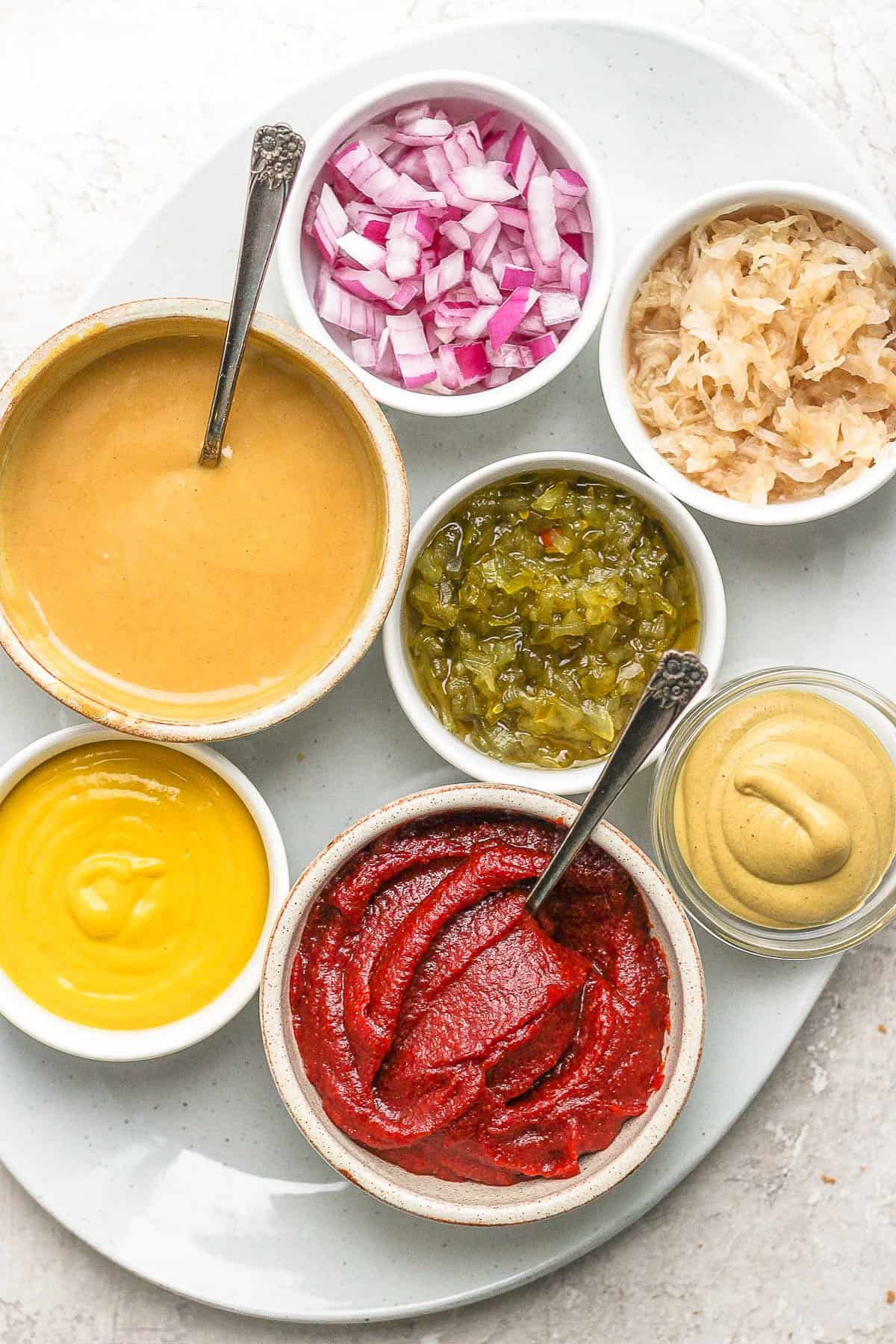 Various condiments in bowls all sitting on a platter. 