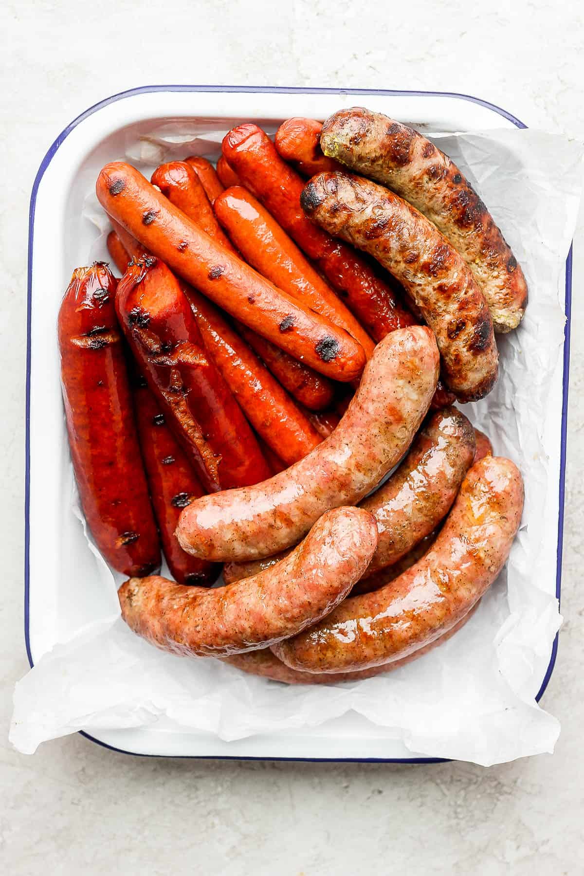 A parchment lined try with smoked brats, smoked hot dogs, grilled hot dogs and grilled brats.