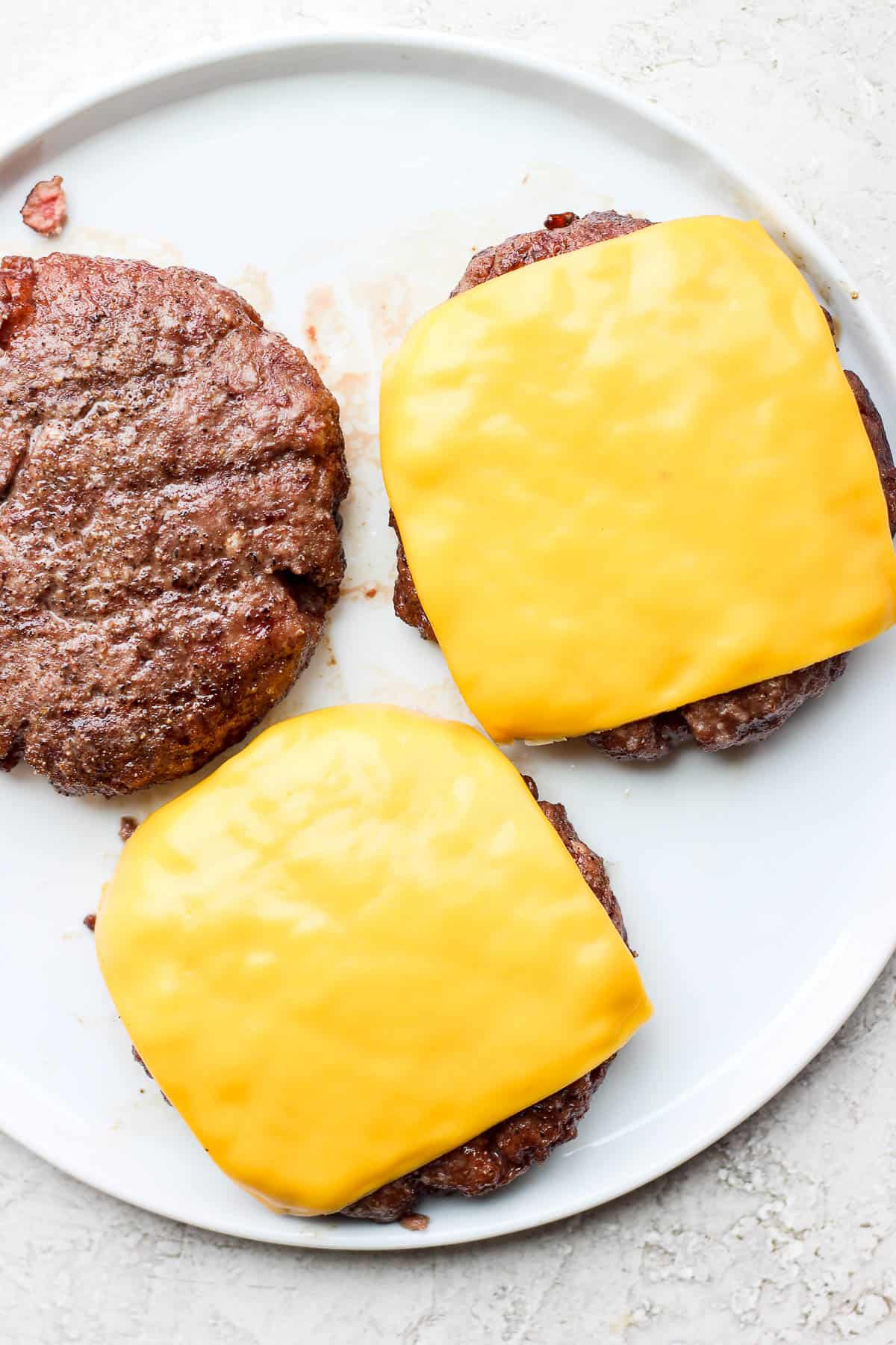Three smoked burgers on a plate, two have cheese on top.