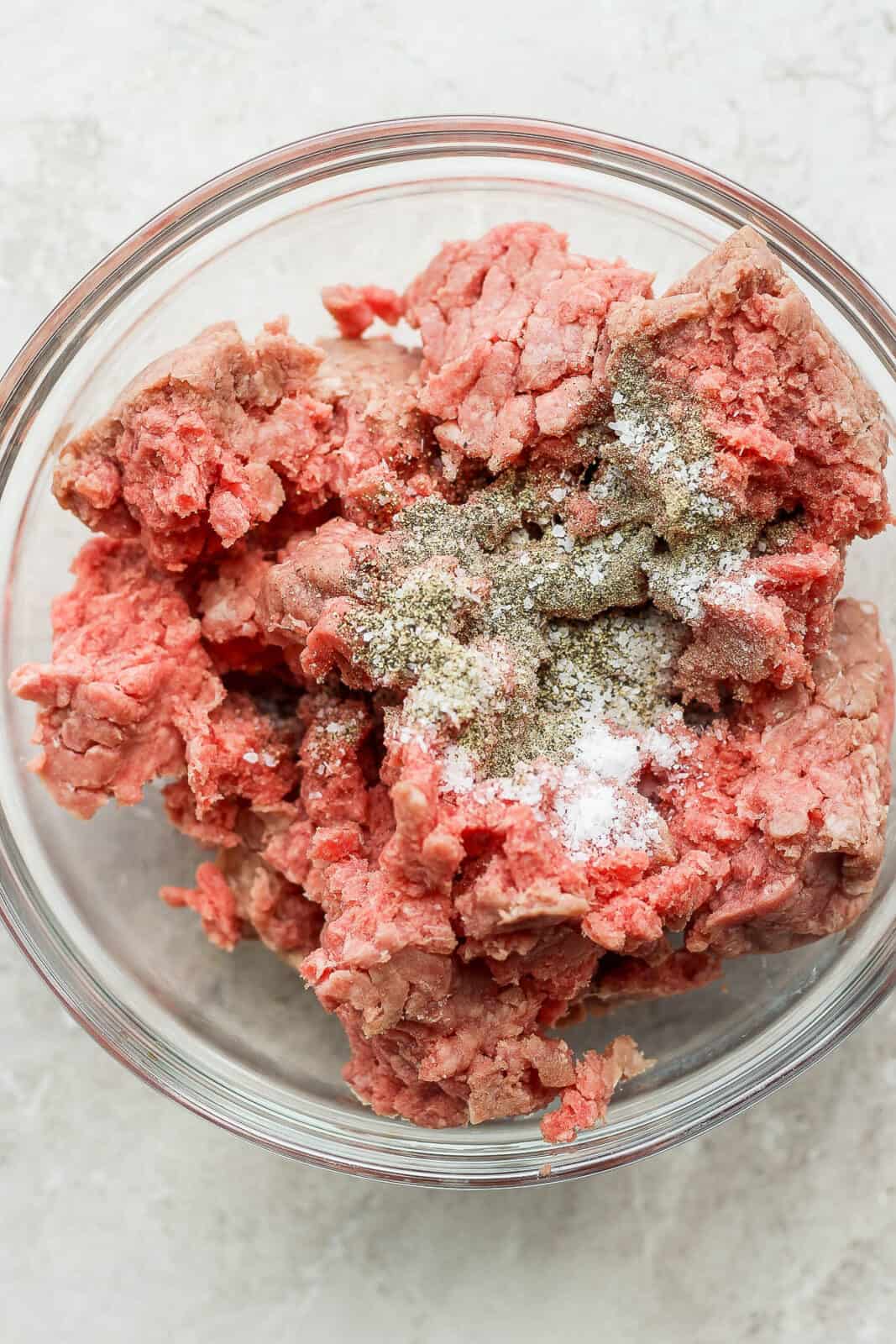 Ground beef in a bowl with salt and pepper. 