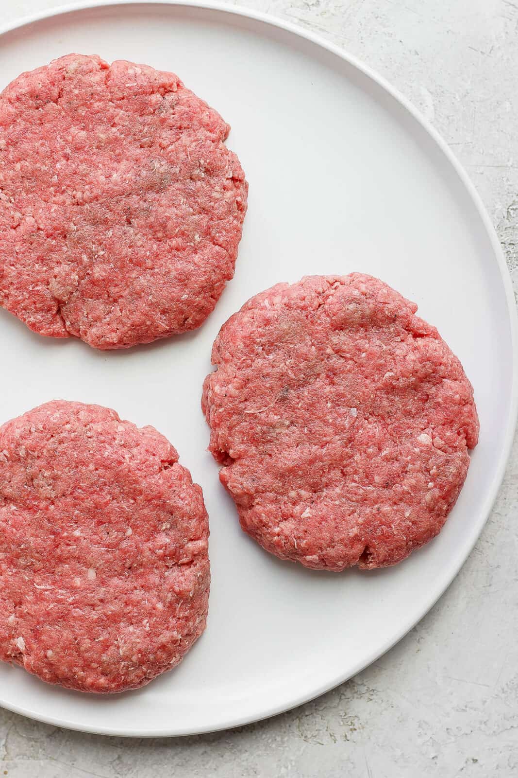 Three raw burger patties on a plate. 