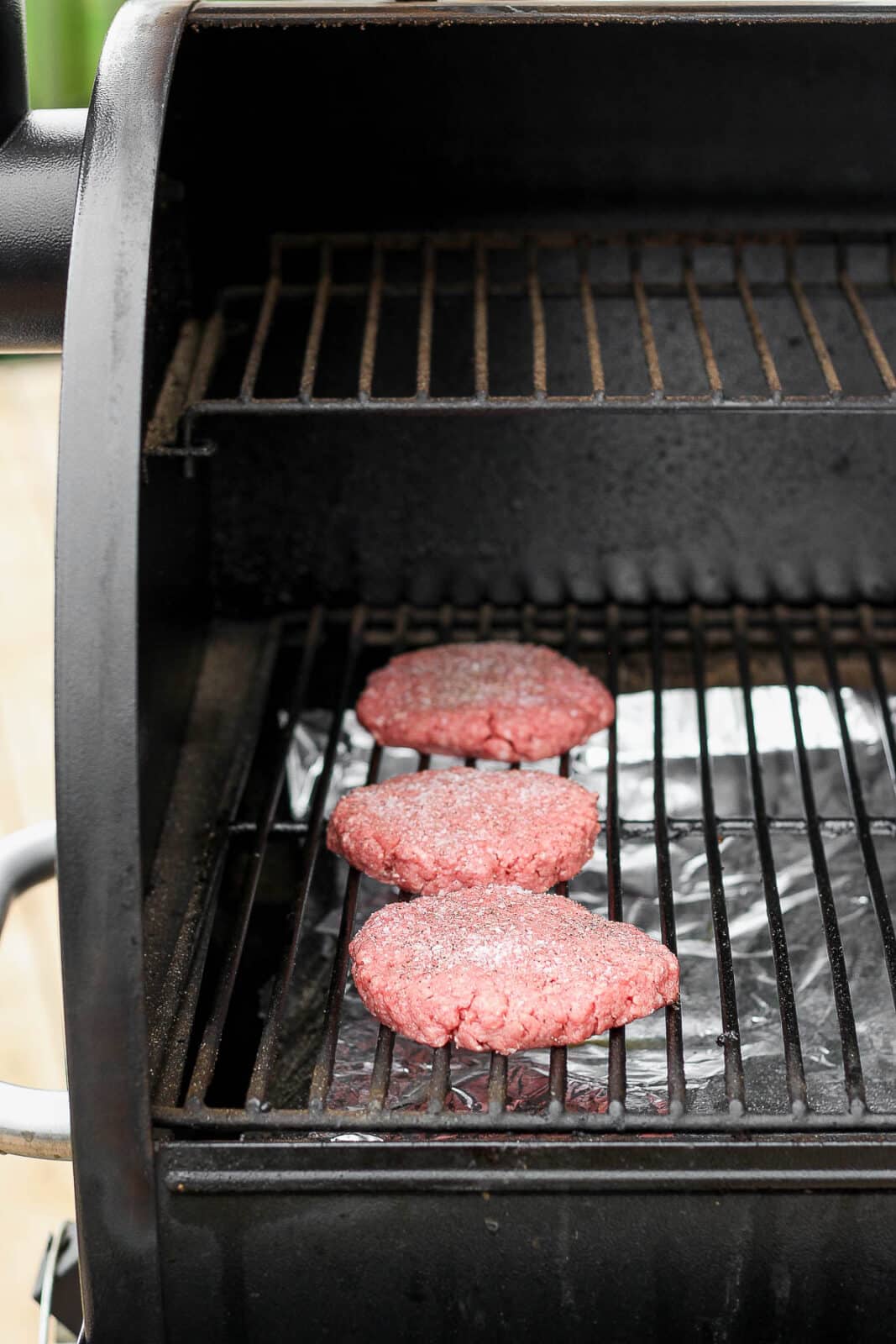 Three raw burger patties on a smoker. 