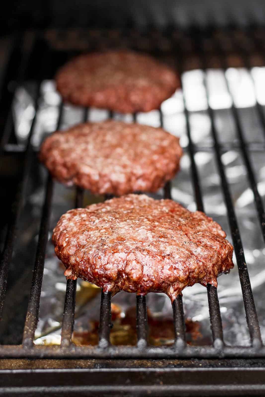 Three smoked burgers on a smoker, fully cooked. 