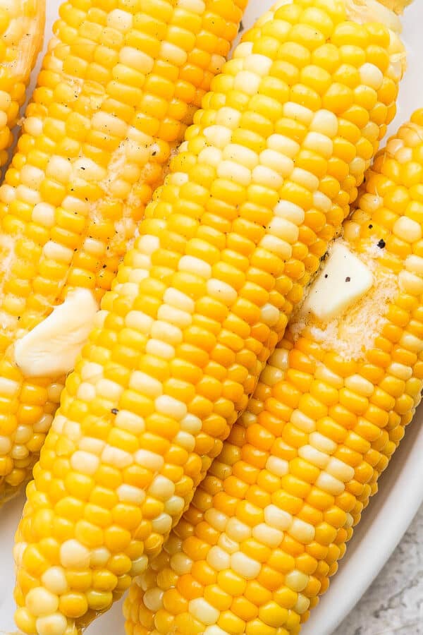 Four ears of smoked corn on the cob on a plate with butter on top.