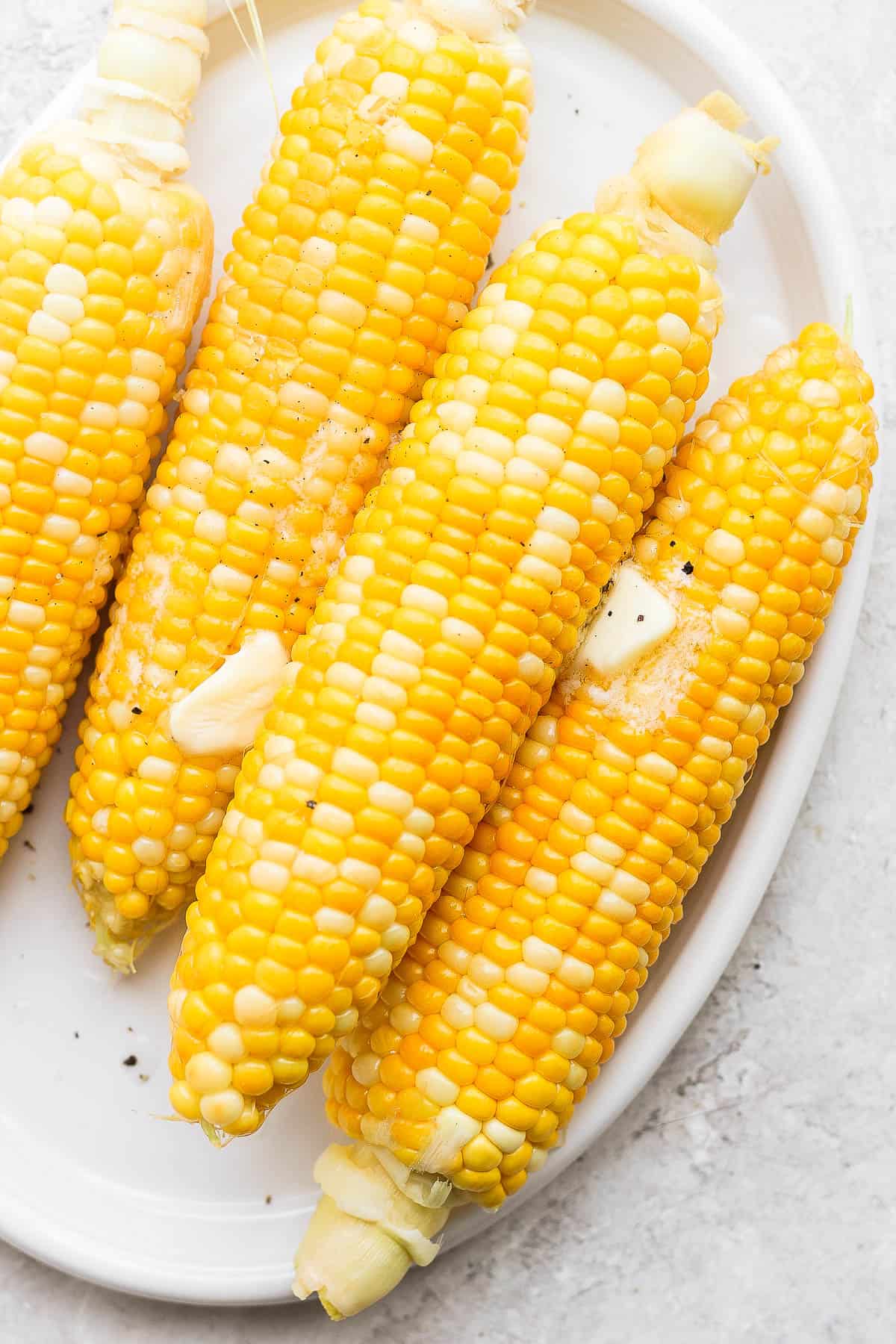 Plate of smoked corn on the cob with butter and salt on top. 