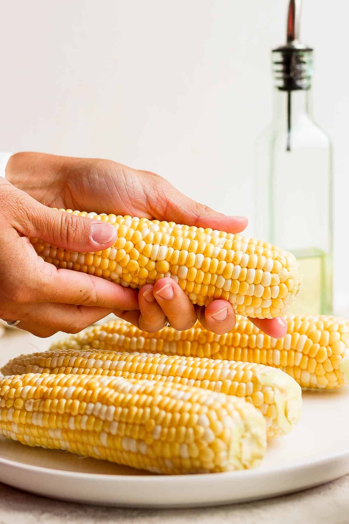 Someone rubbing oil on a piece of shucked corn.