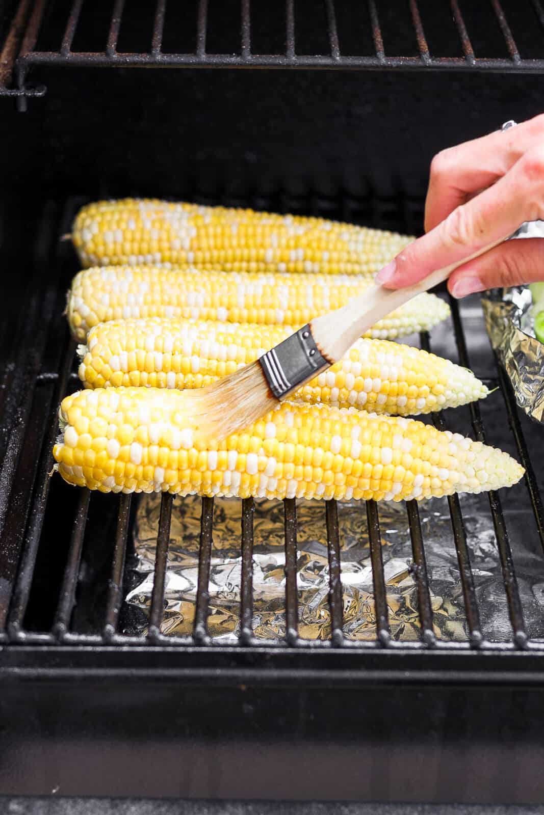 Corn on the smoker with someone brushing with olive oil. 