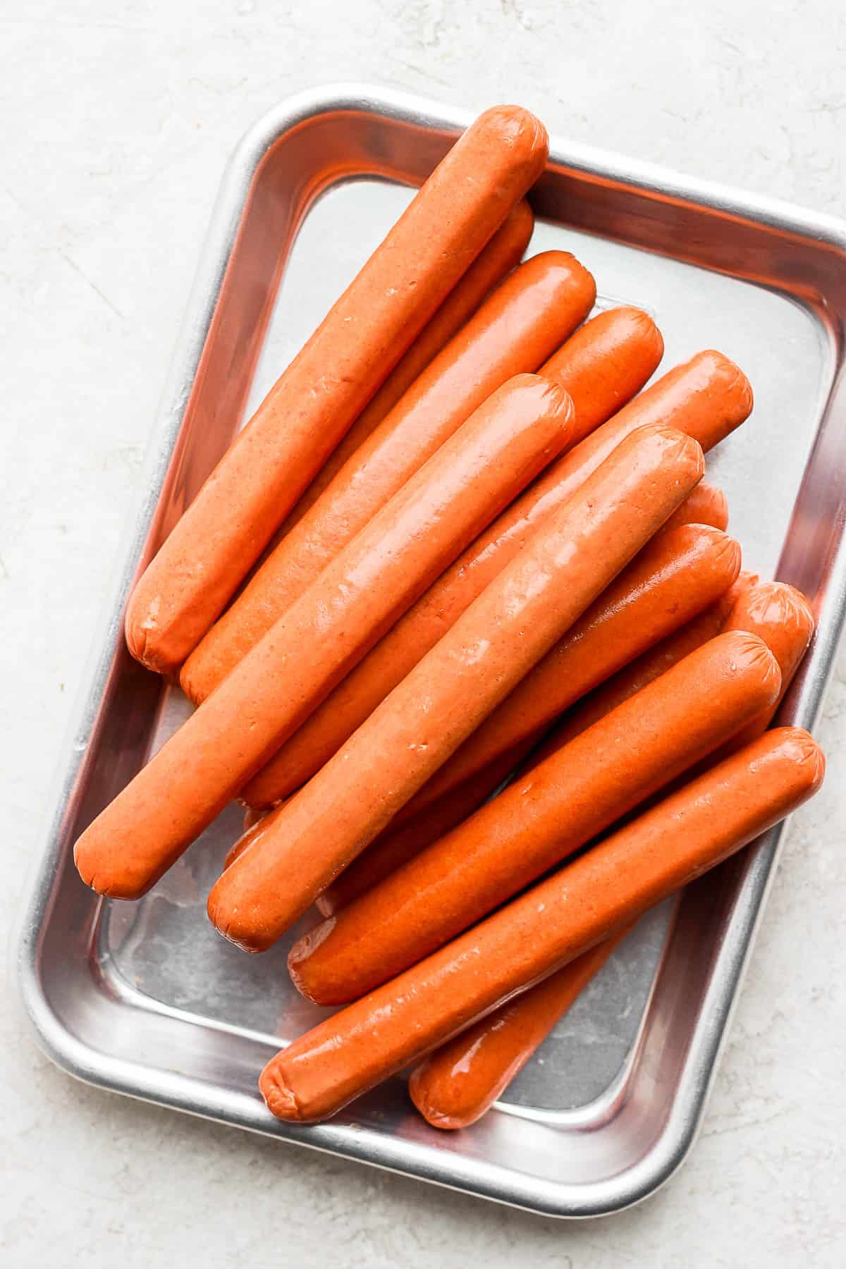 Uncooked hot dogs on a small metal platter.