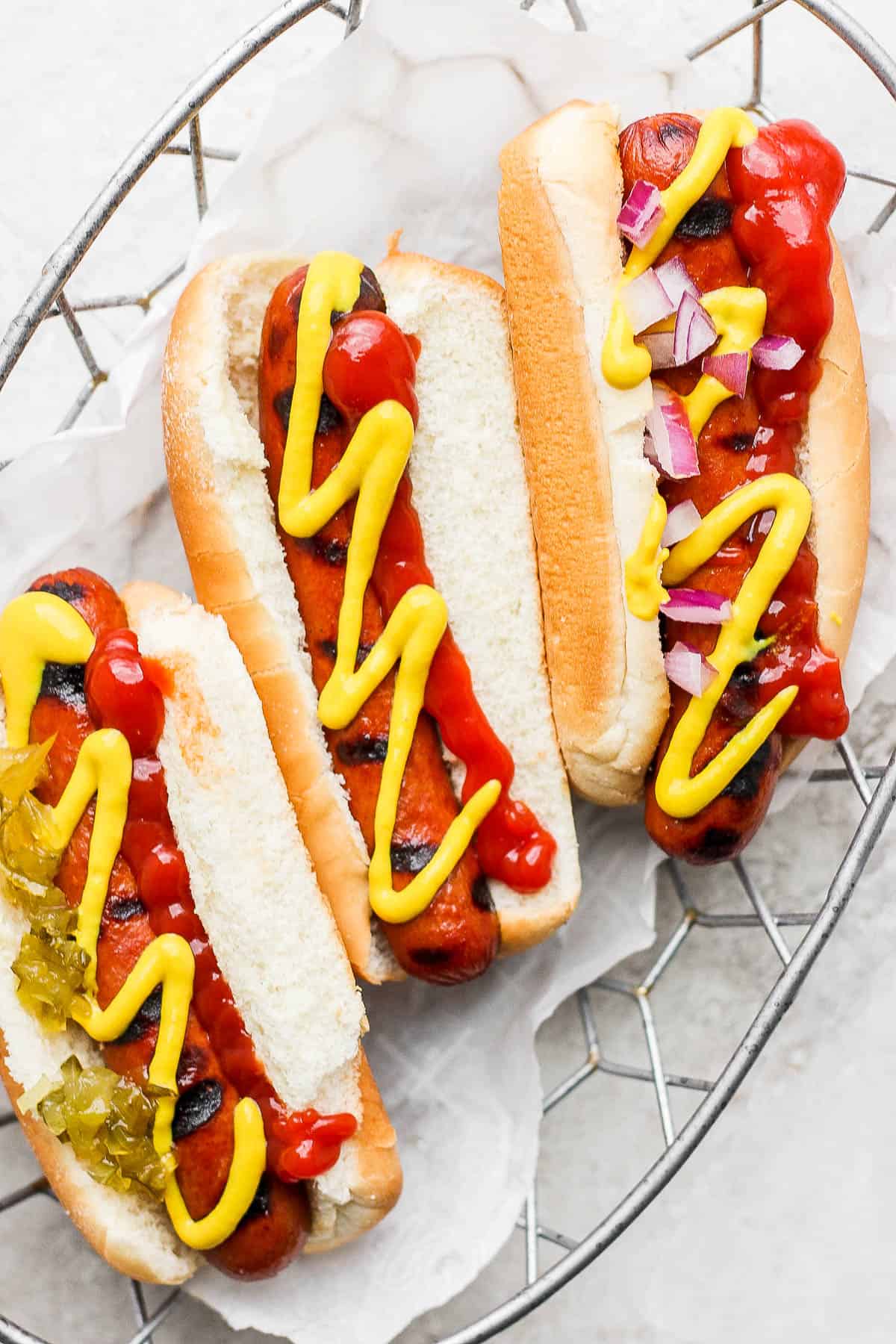 Three smoked hot dogs topped with ketchup and mustard in a parchment lined wire basket.