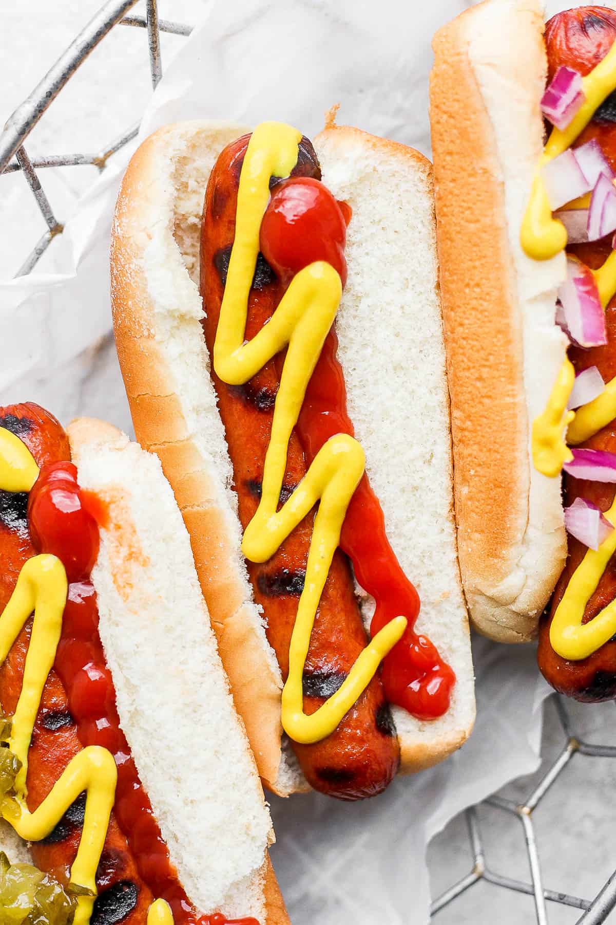 Three smoked hot dogs topped with ketchup and mustard in a parchment lined wire basket.