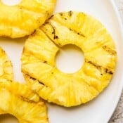 A slice of grilled pineapple surrounded by more grilled pineapple on a white plate.