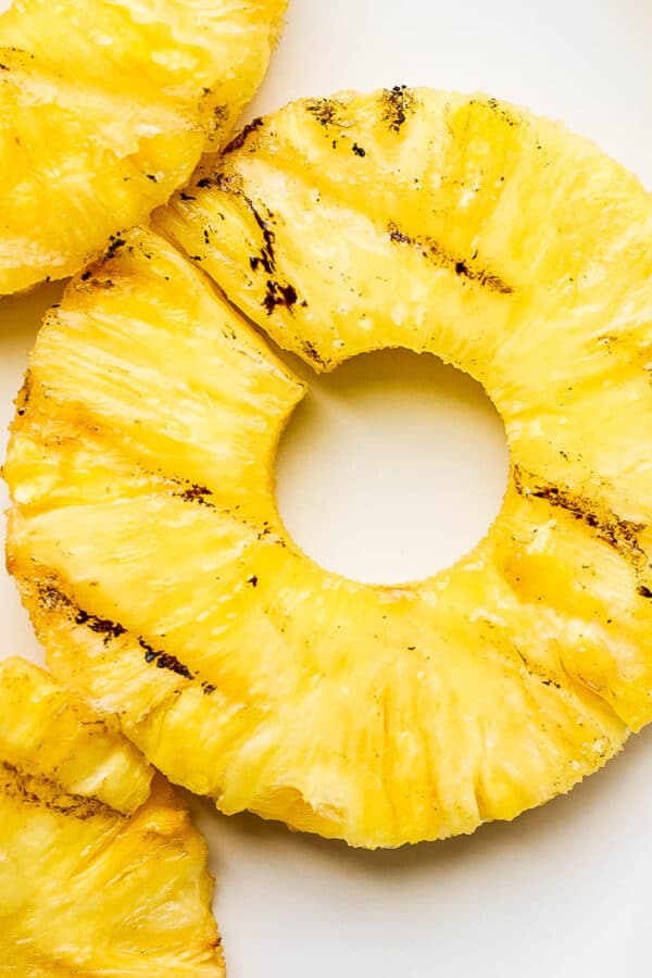 A slice of grilled pineapple surrounded by more grilled pineapple on a white plate.