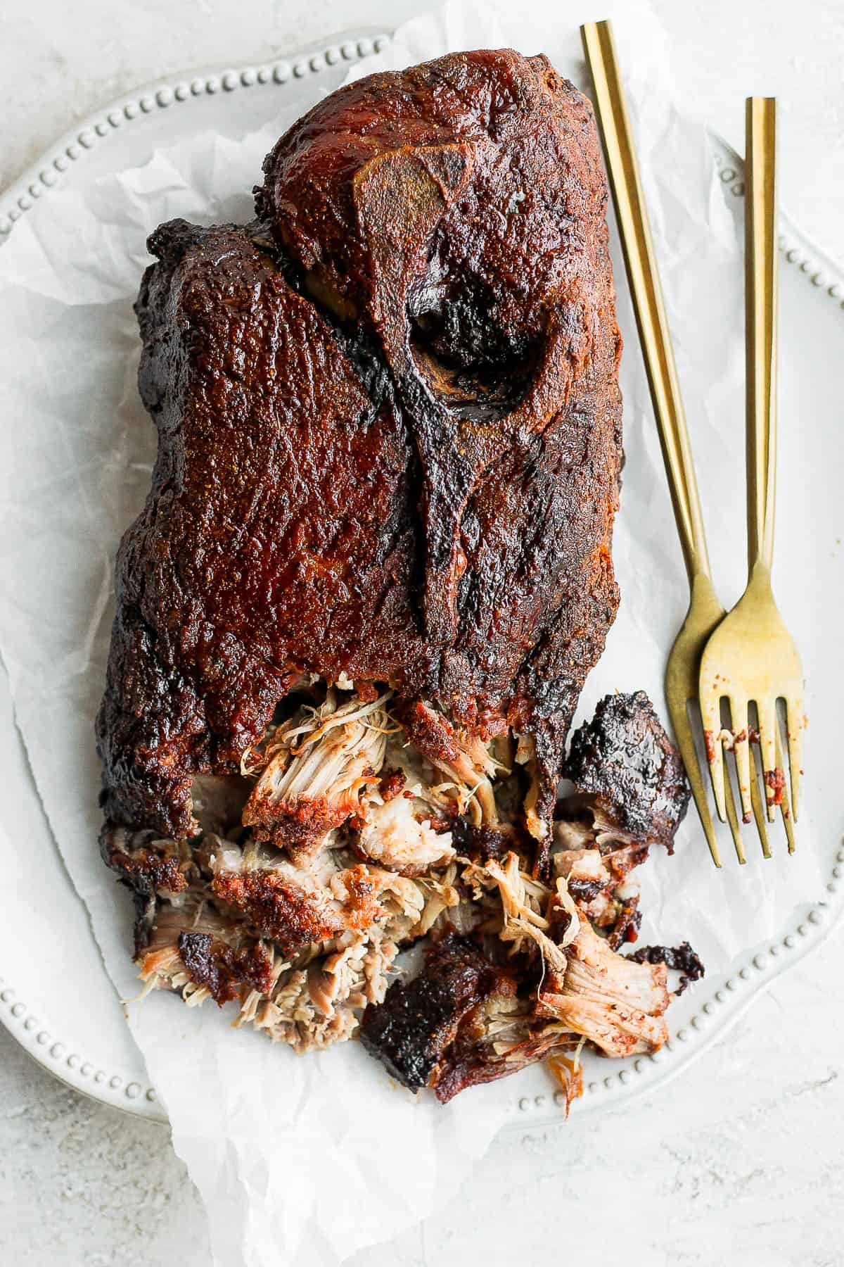 A smoked pork butt on a plate with the front portion shredded.