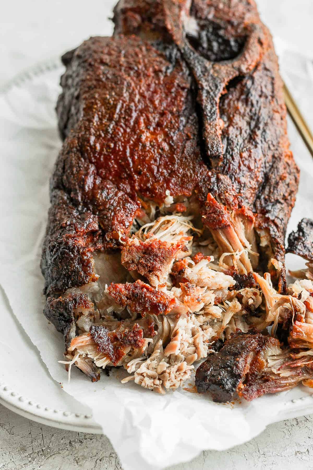 A smoked pork butt on a plate with the front portion shredded.