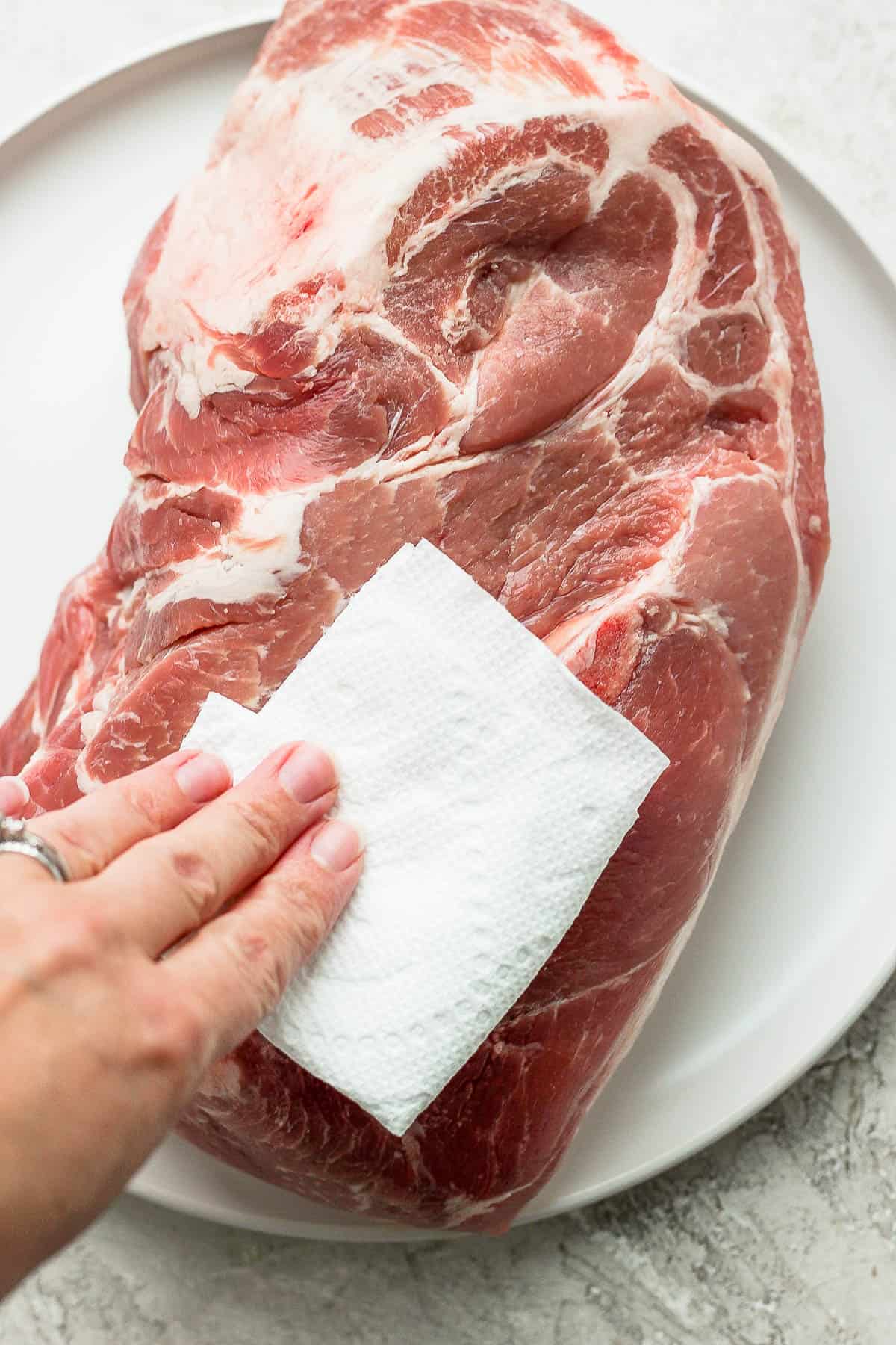 Someone patting a pork butt dry with a clean paper towel.