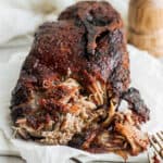 A smoked pork butt on a parchment lined plate with part of it shredded.