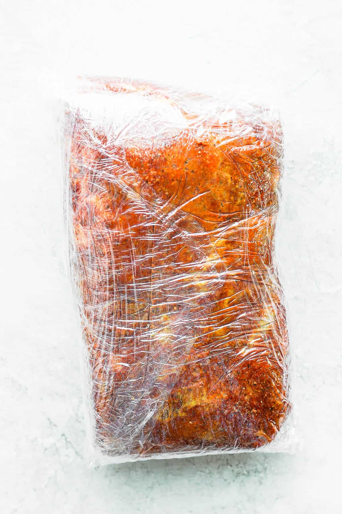 Prepared pork butt wrapped in plastic wrap.