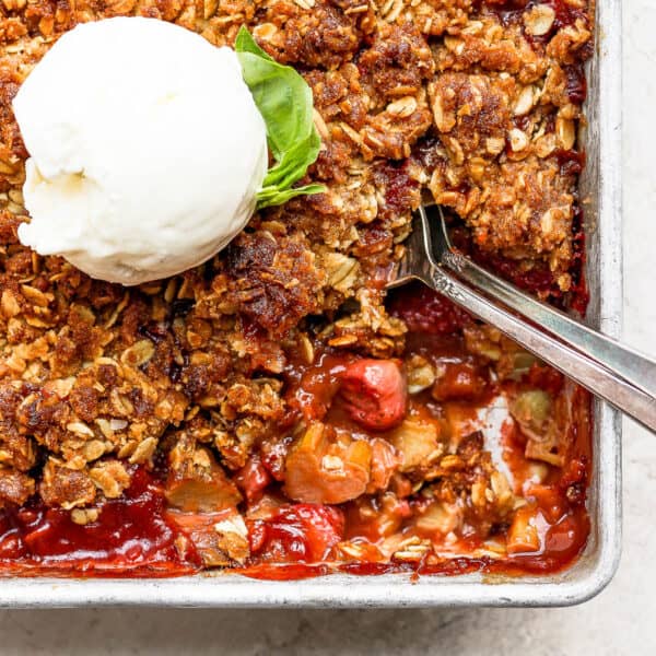 Pan of strawberry rhubarb crisp topped with ice cream and two spoons sticking out.