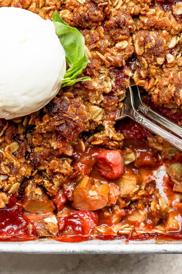 Pan of strawberry rhubarb crisp topped with ice cream and two spoons sticking out.